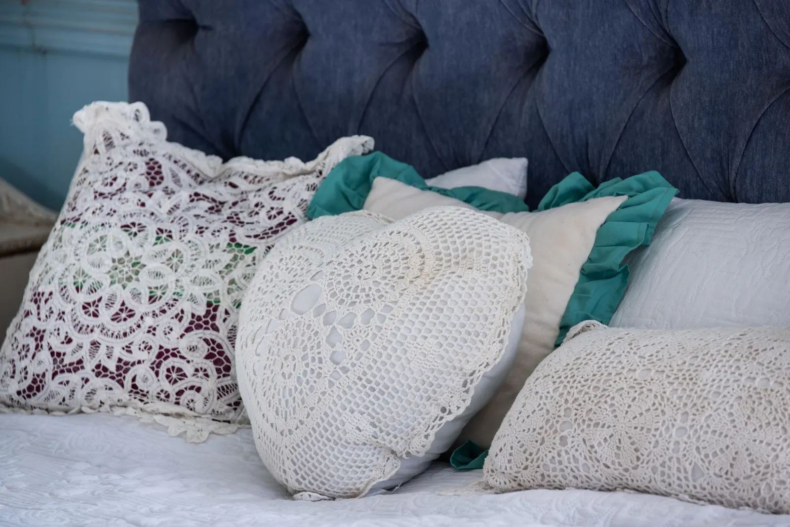 Elegant lace pillows on a bed with a tufted headboard. Perfect for cozy and vintage home decor themes.