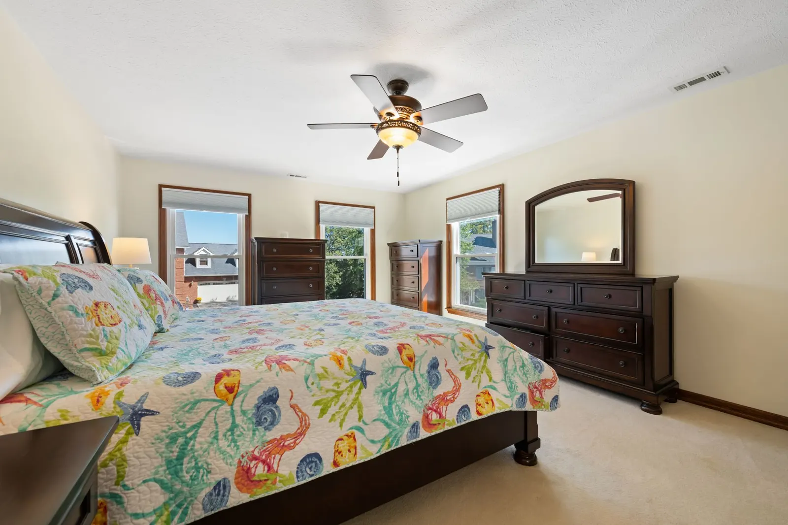 Sunny bedroom with vibrant bedding, dark wooden furniture, and ceiling fan for a cozy feel.