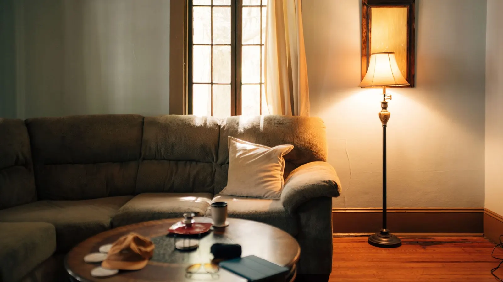 Living room with a gray sofa, a round coffee table and a lit floor lamp by the window