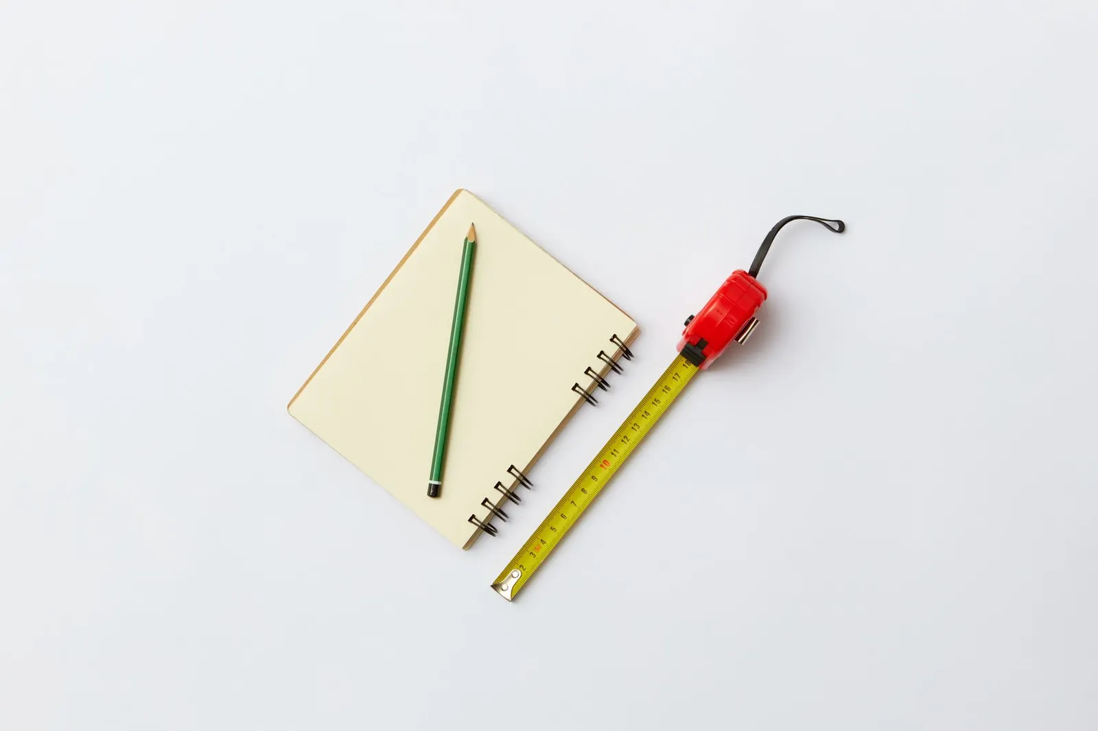 Tape measure, notebook and paint swatches on a wood floor beside an empty white living room wall