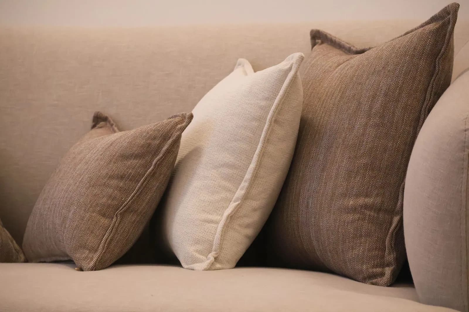Cream sofa with linen, boucle and knit pillows, a chunky wool throw and a woven basket beside it