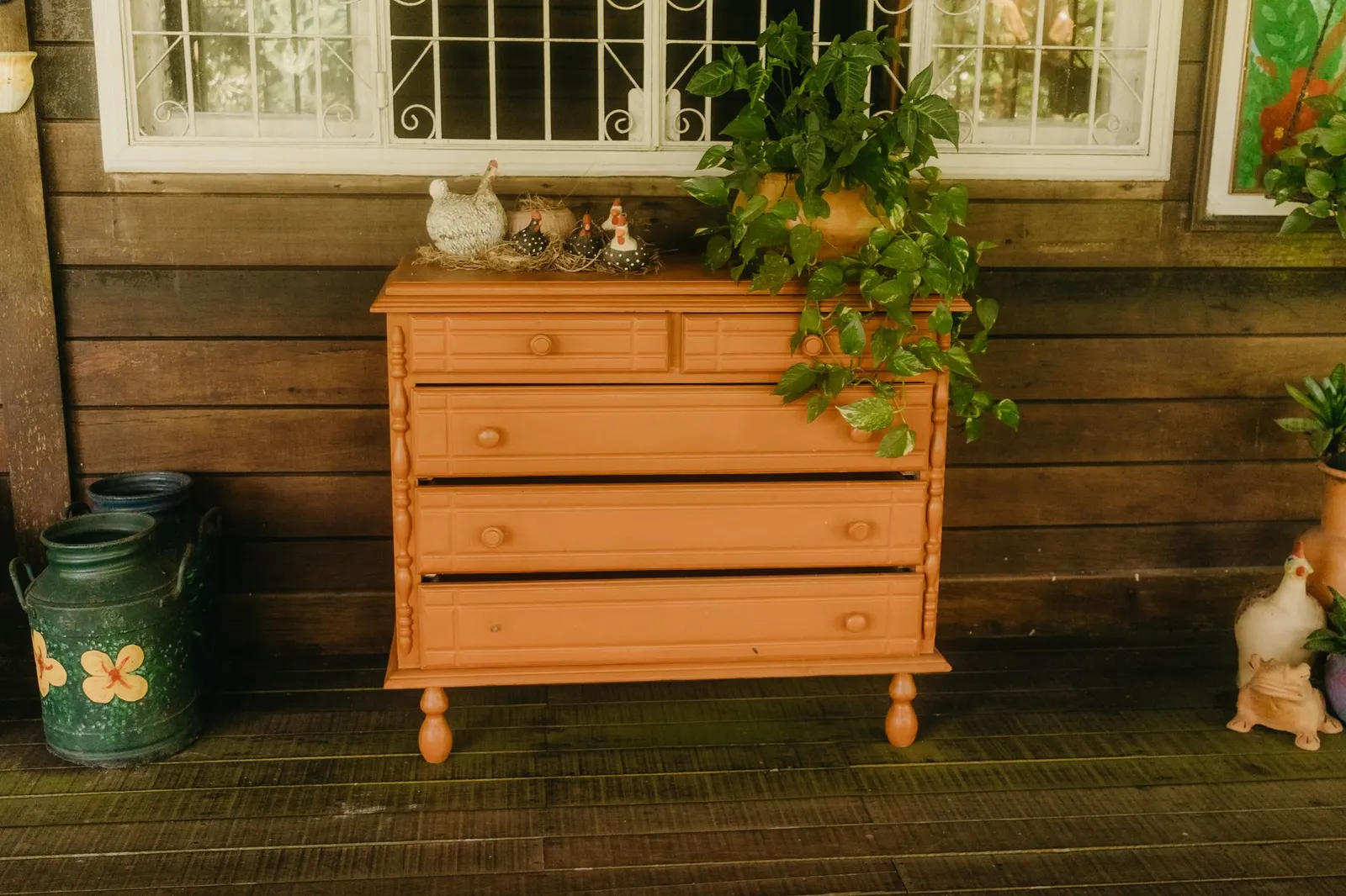 Painted thrifted wood dresser with brass pulls, a ceramic lamp, a stack of books and a leaning round mirror
