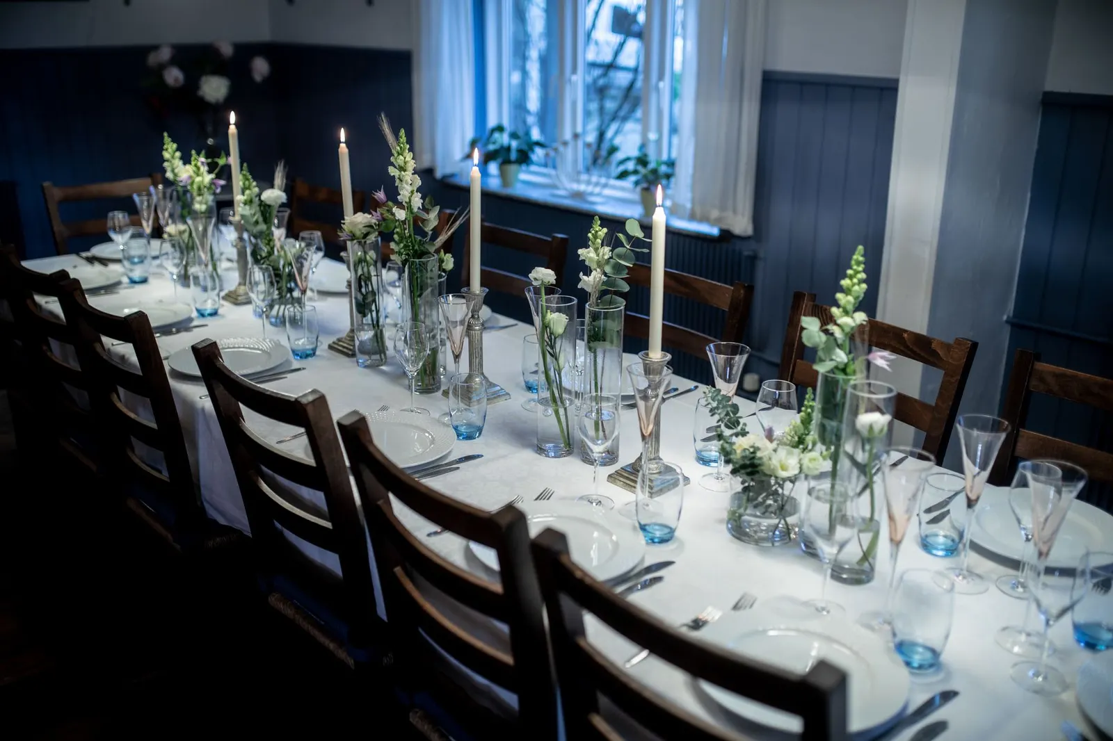Table set with a white cloth, blue napkins, silver votives and scattered gold chocolate coins