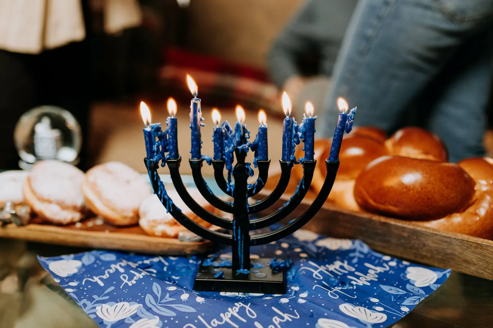 Lit menorah standing on a metal tray on a kitchen counter, well away from curtains