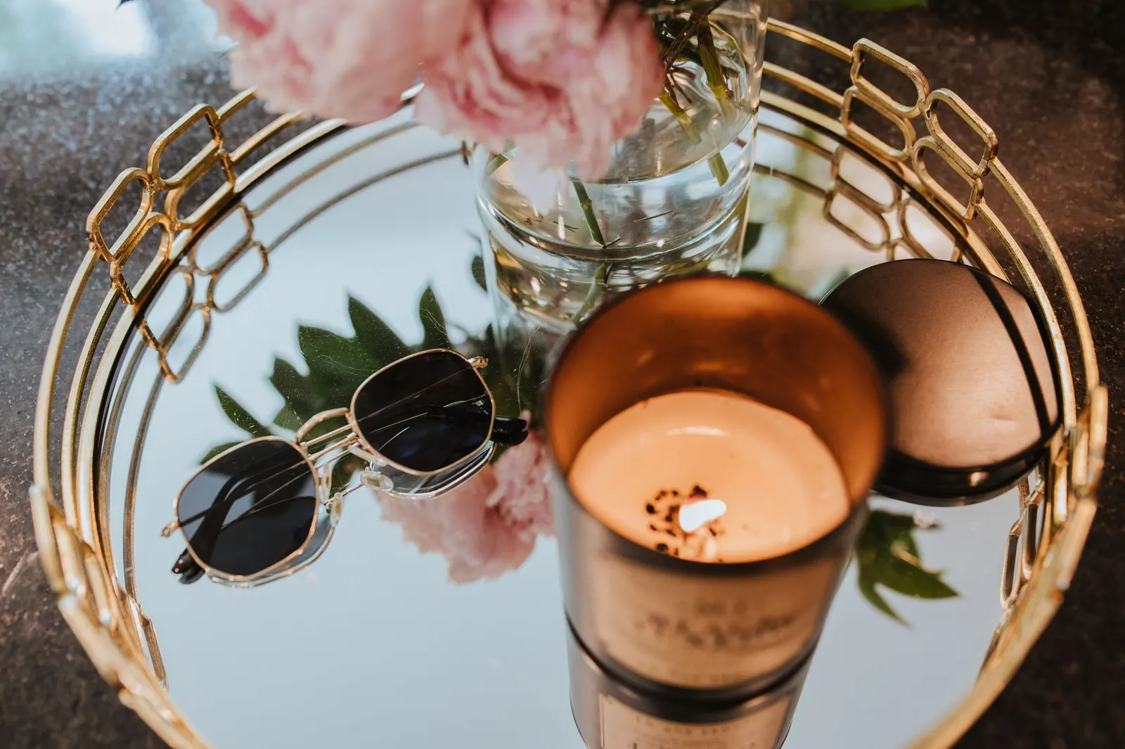 Round mirror tray with a gold rim holding perfume bottles and a small candle on a dresser