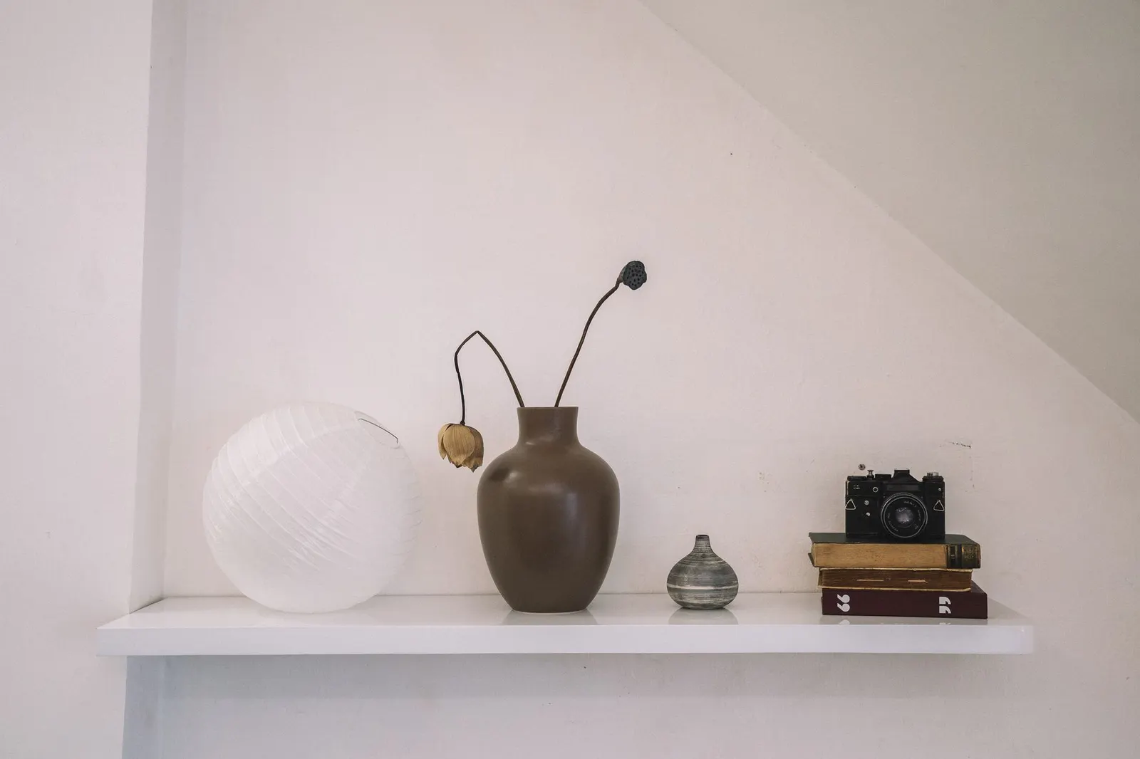 Shelf vignette with a tall stone-look vase, black candle holder, stacked books and a small plant
