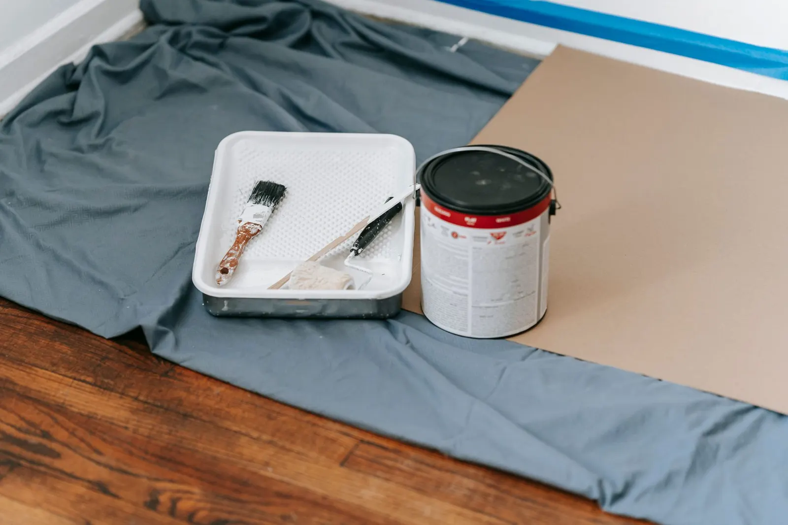 Small wood nightstand on a drop cloth with drawer removed, a paint can and brush beside it