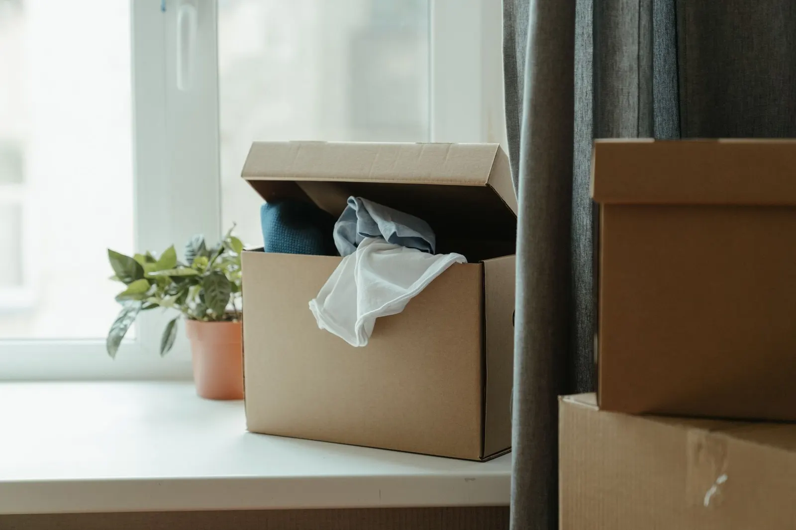 Open cardboard box with toilet paper, cleaning spray, a tool kit and a power strip on a wood floor