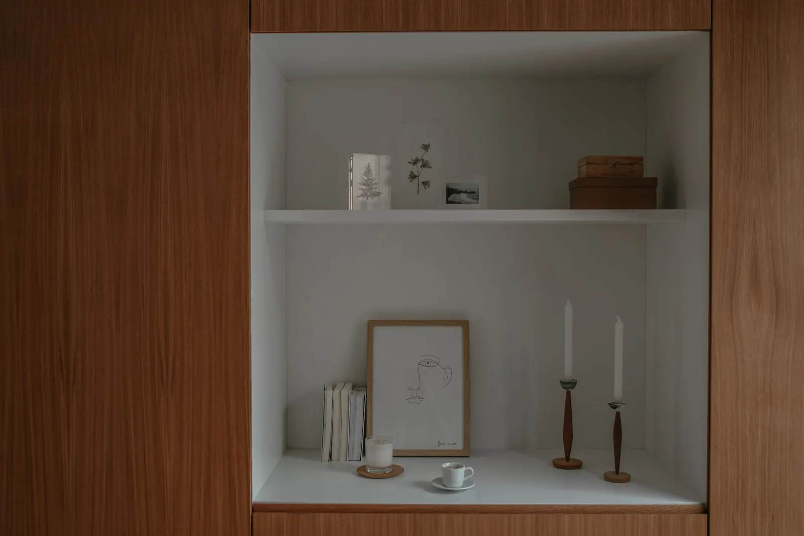 White built-in shelf with unlit taper candles, a framed print and small decor