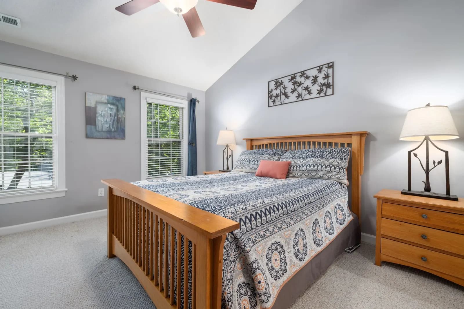 Small guest bedroom with a made bed, white sheets, two extra pillows, a knit throw and a bedside lamp