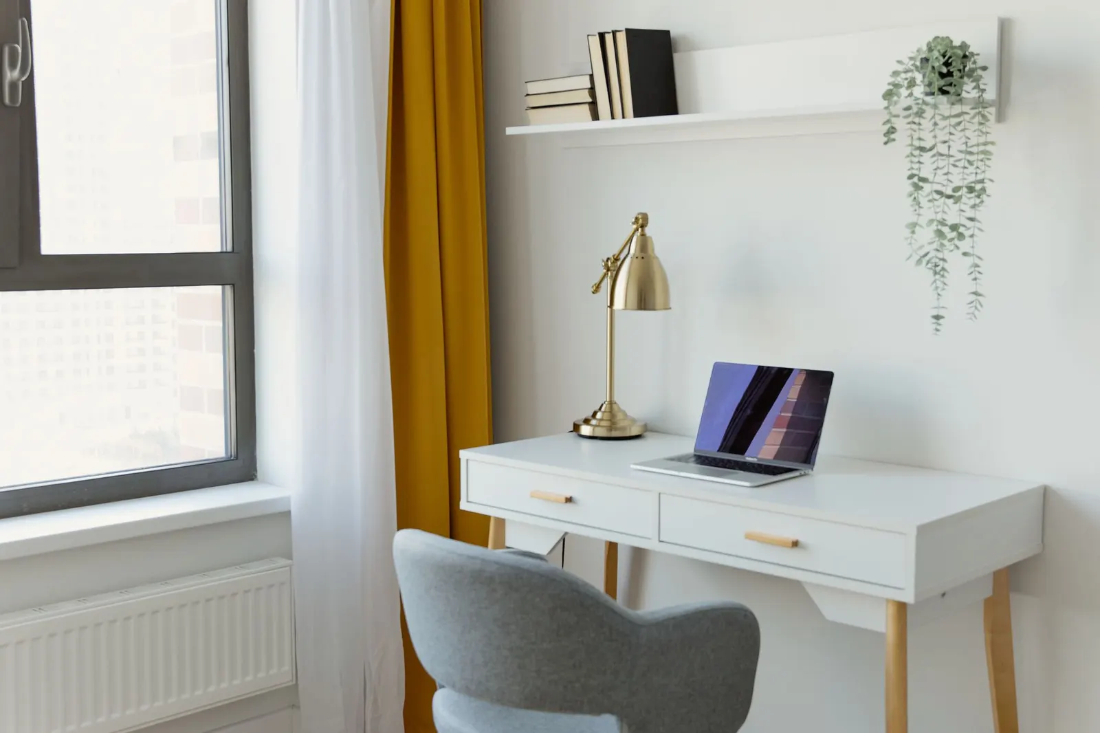 Small home office with a white desk, a brass desk lamp and a window
