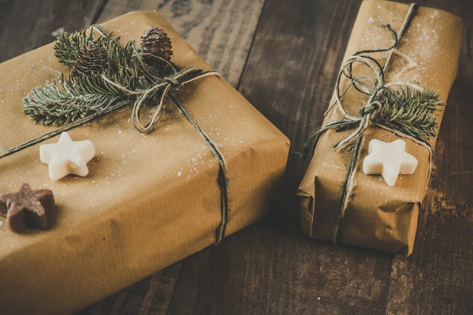 Two gifts wrapped in brown kraft paper with twine and pine sprigs on a wood table