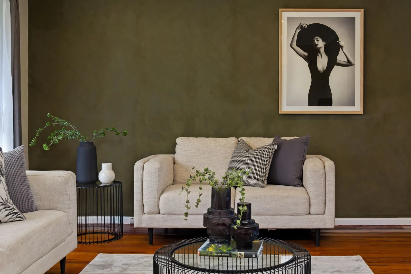 Living room with an olive green wall, cream linen sofa, rust pillows and a walnut side table