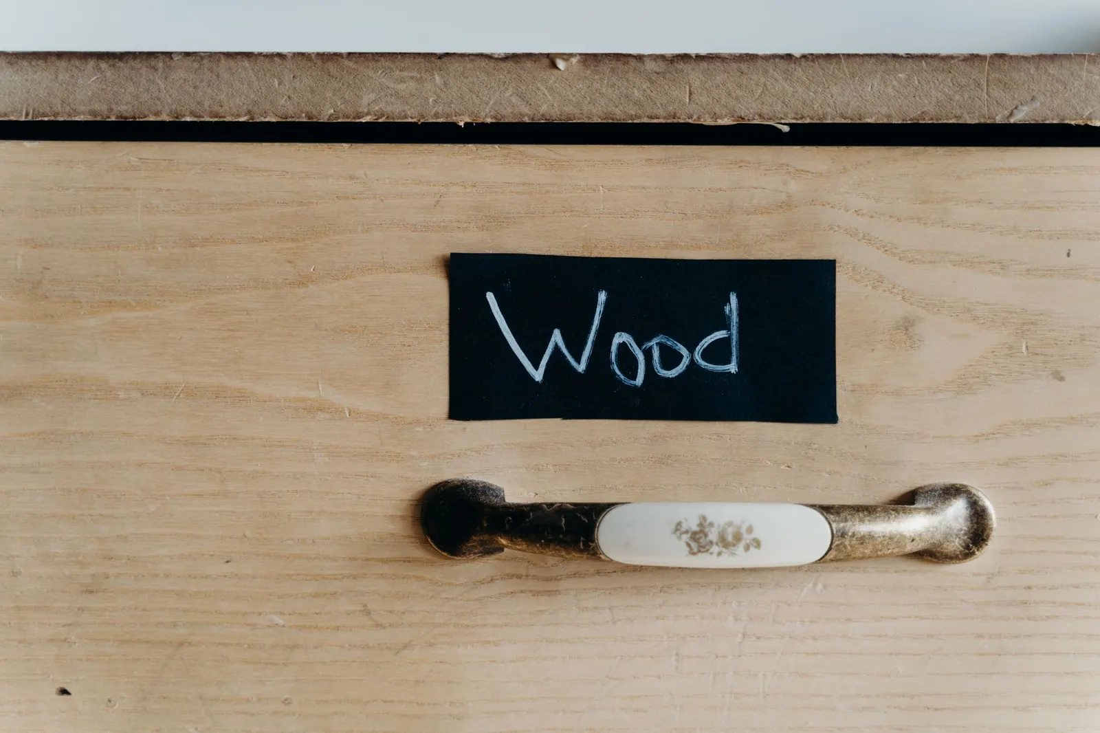 Detailed view of a wooden cabinet drawer with chalk-labeled sign and vintage handle.