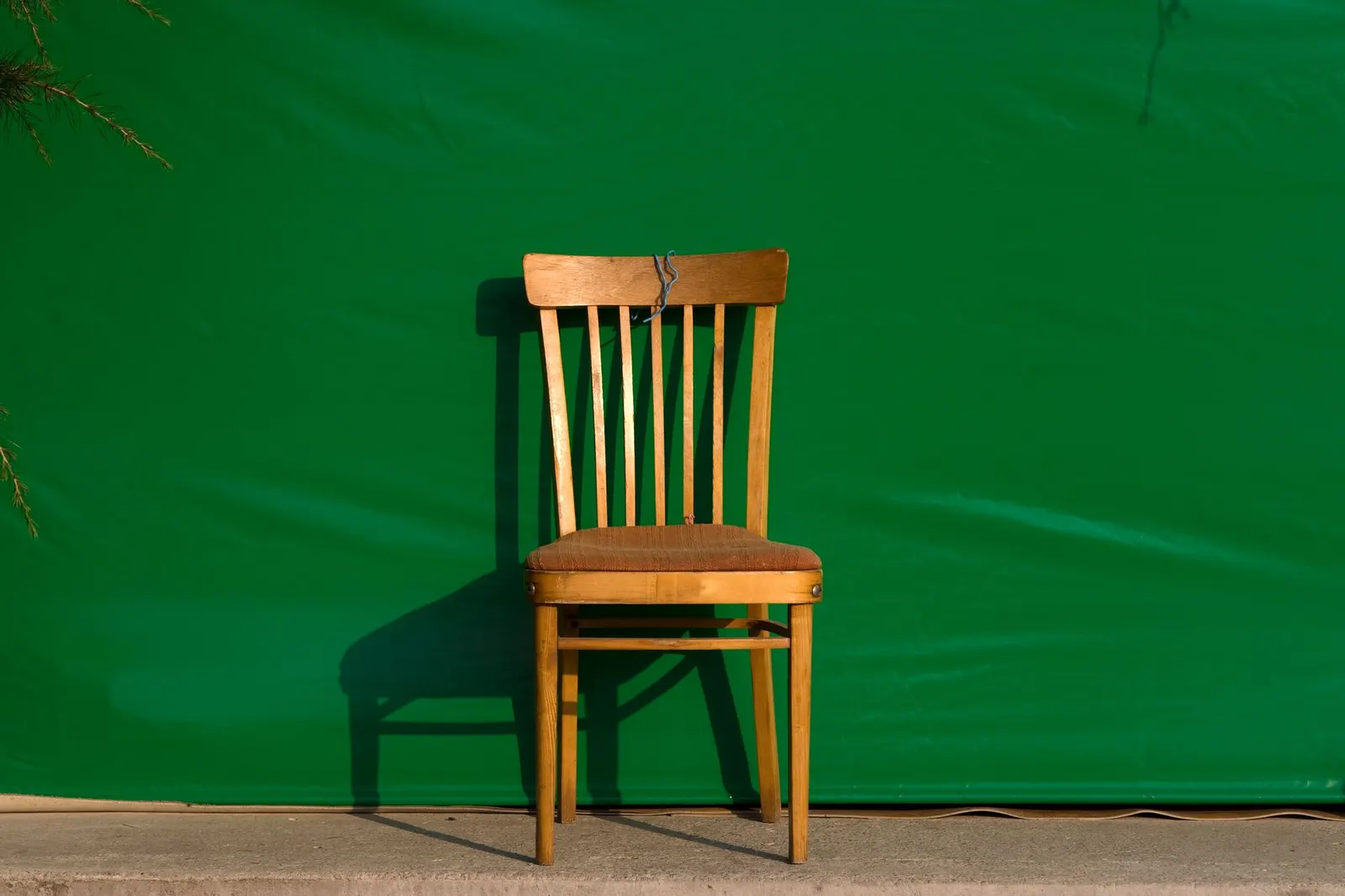 A solitary vintage wooden chair set against a vibrant green background.