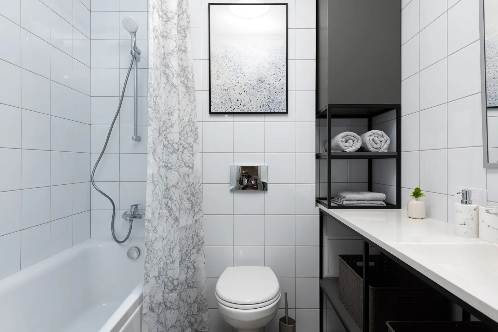 Interior of light bathroom with toilet near bathtub with shower and curtain near counter with shelves with towels and containers and decorative objects near w