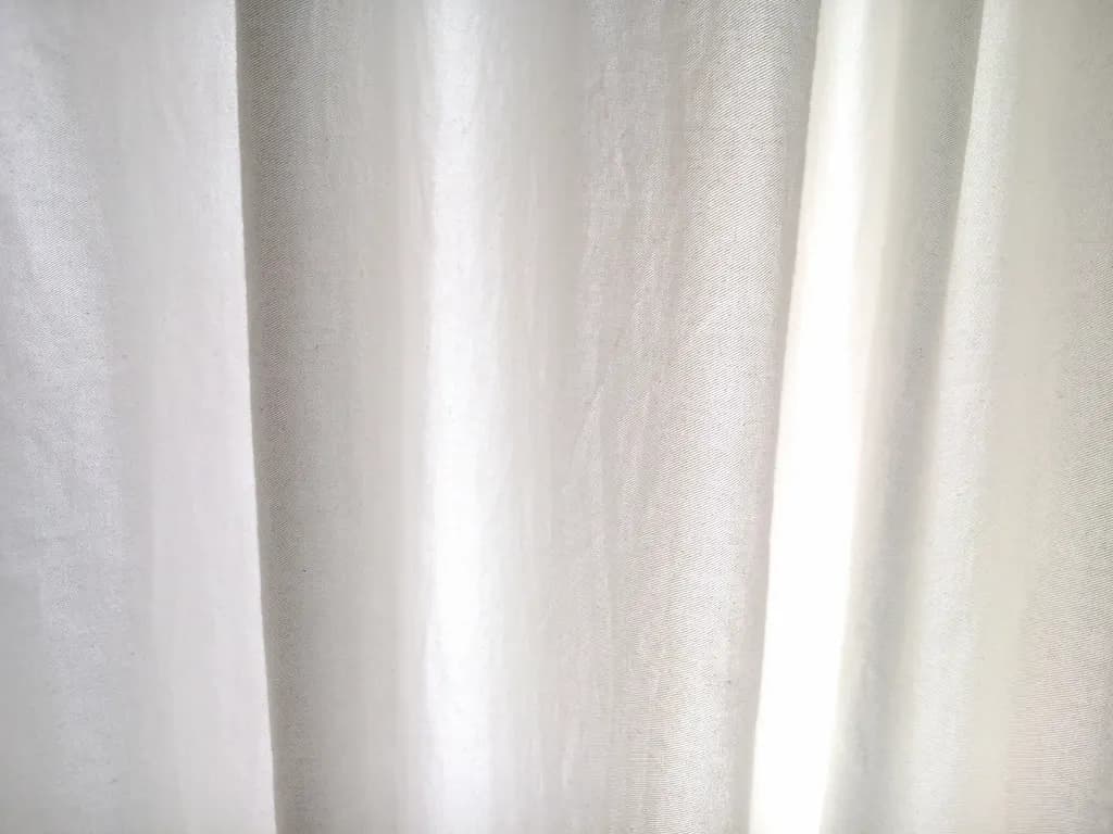 White linen curtains hung high on a slim rod beside a sunny apartment window