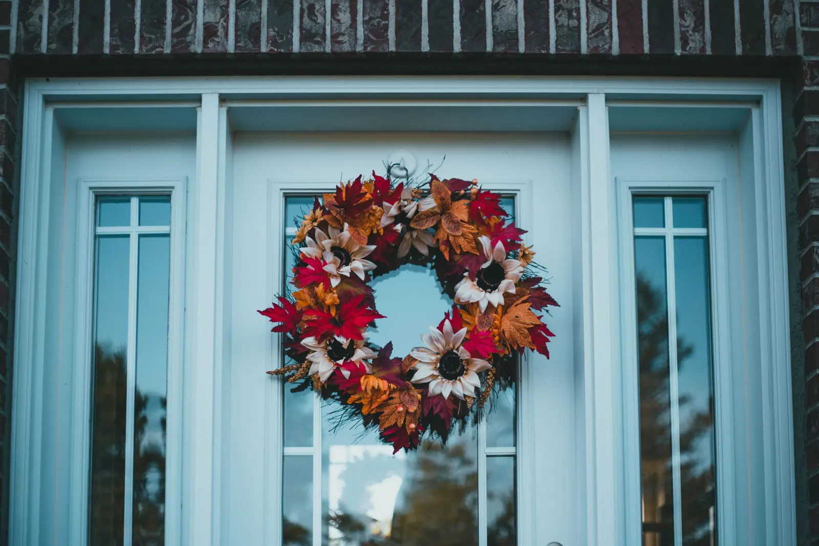 Colorful autumn wreath hanging on a blue front door with glass panels