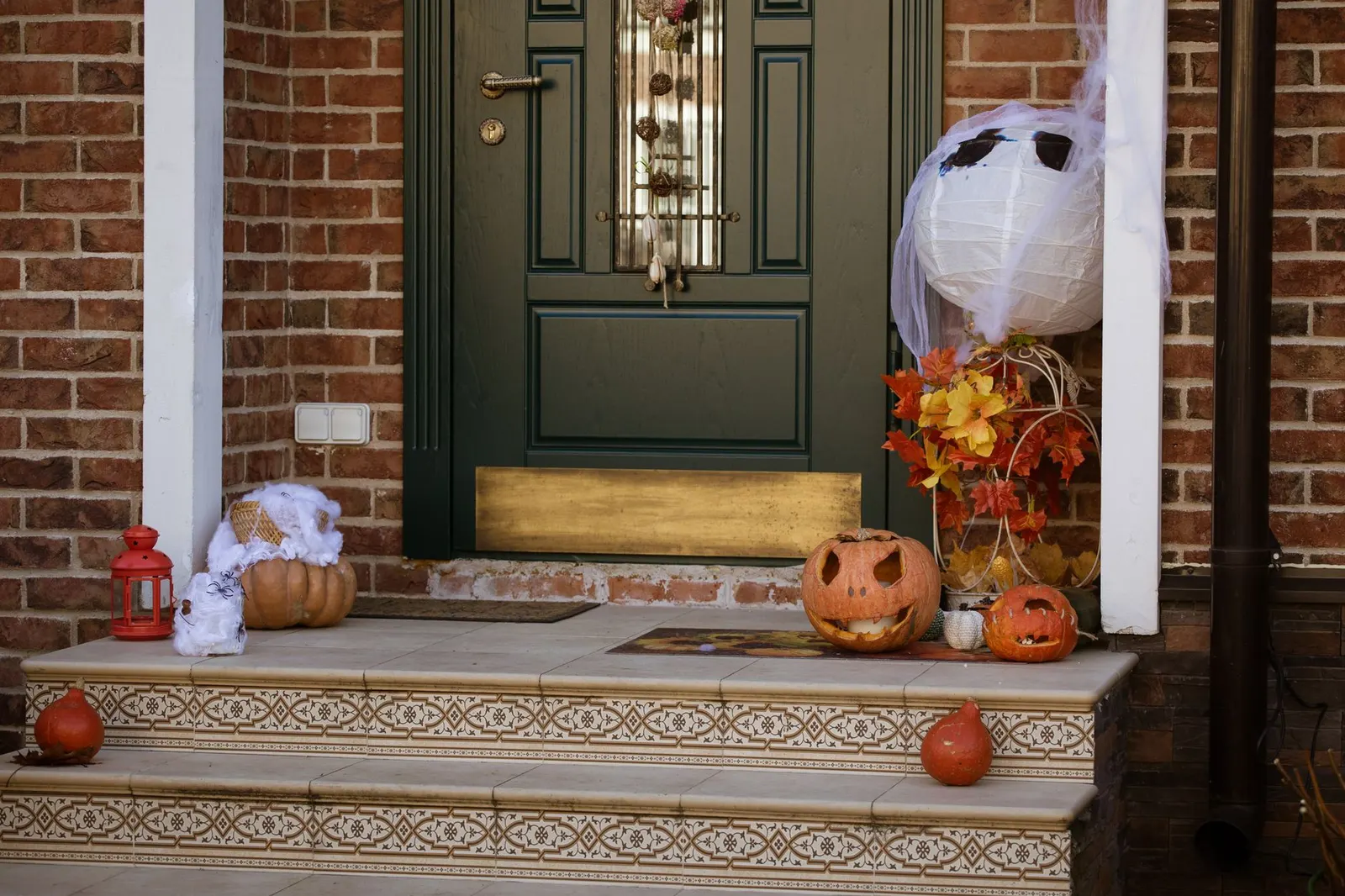 Brick entrance steps decorated with carved pumpkins, autumn leaves and a ghost by a dark front door