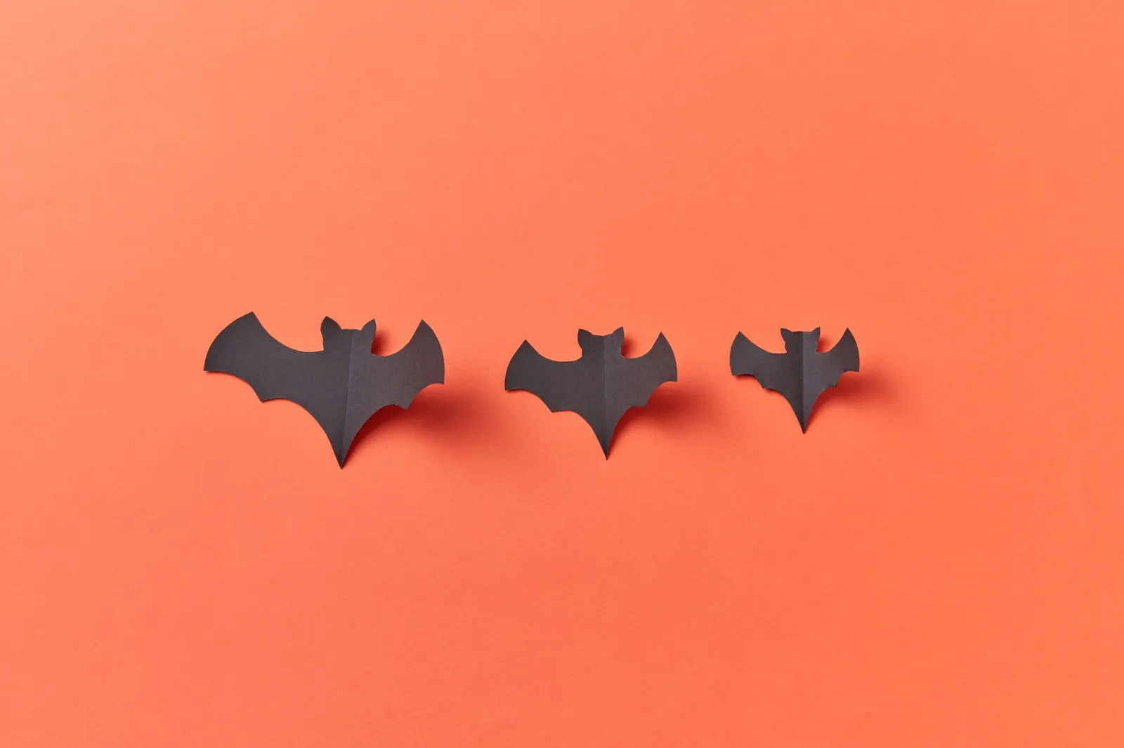 Three black paper bat cutouts on an orange background