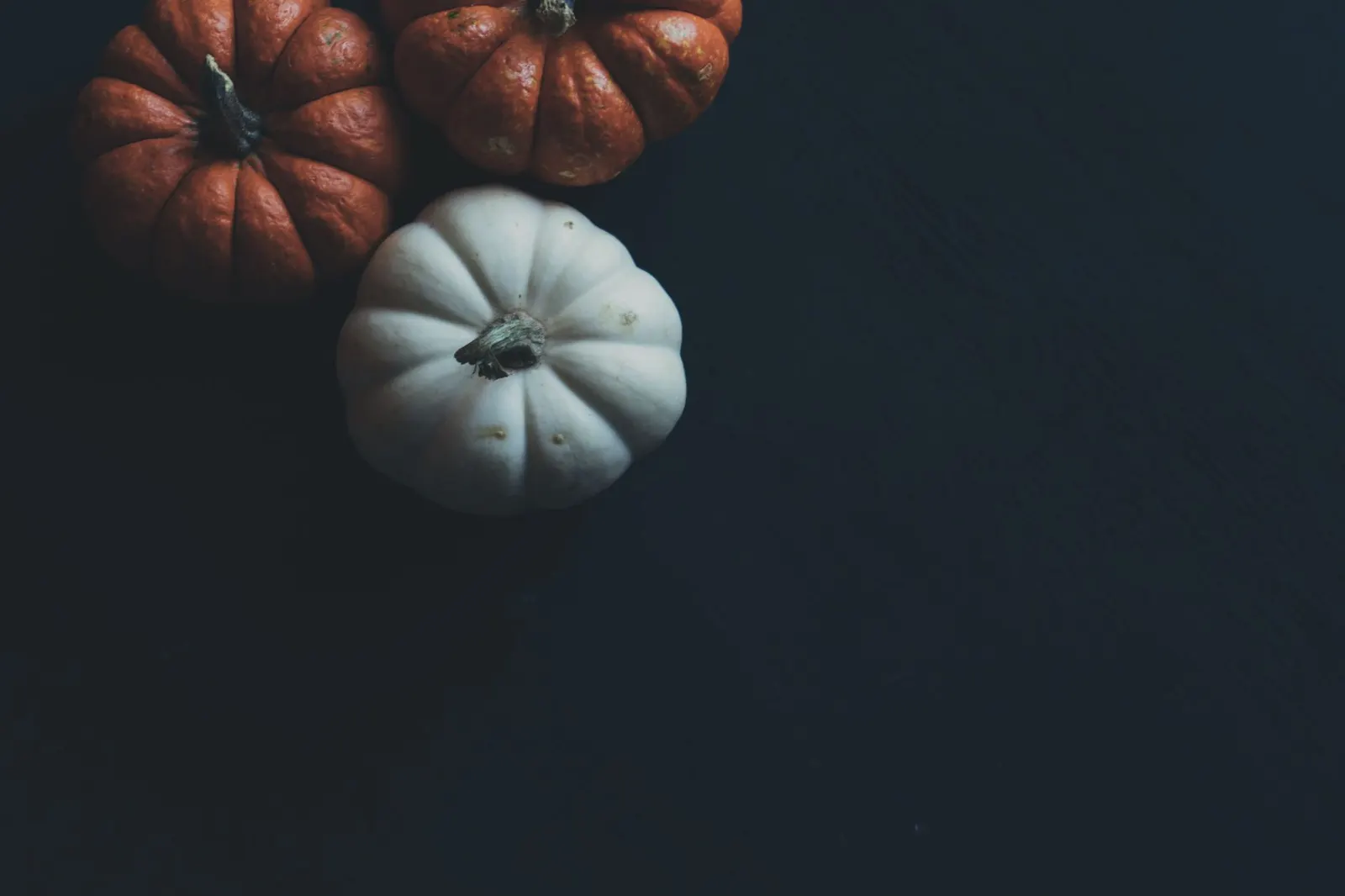 Three mini pumpkins, two orange and one white, on a dark surface