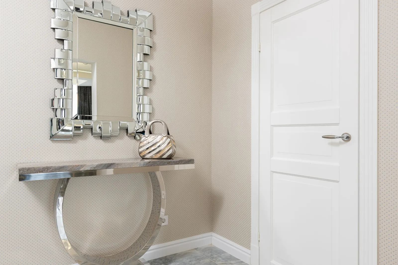 Creative design of hall with handbag on table under mirror in decorative frame against door at home