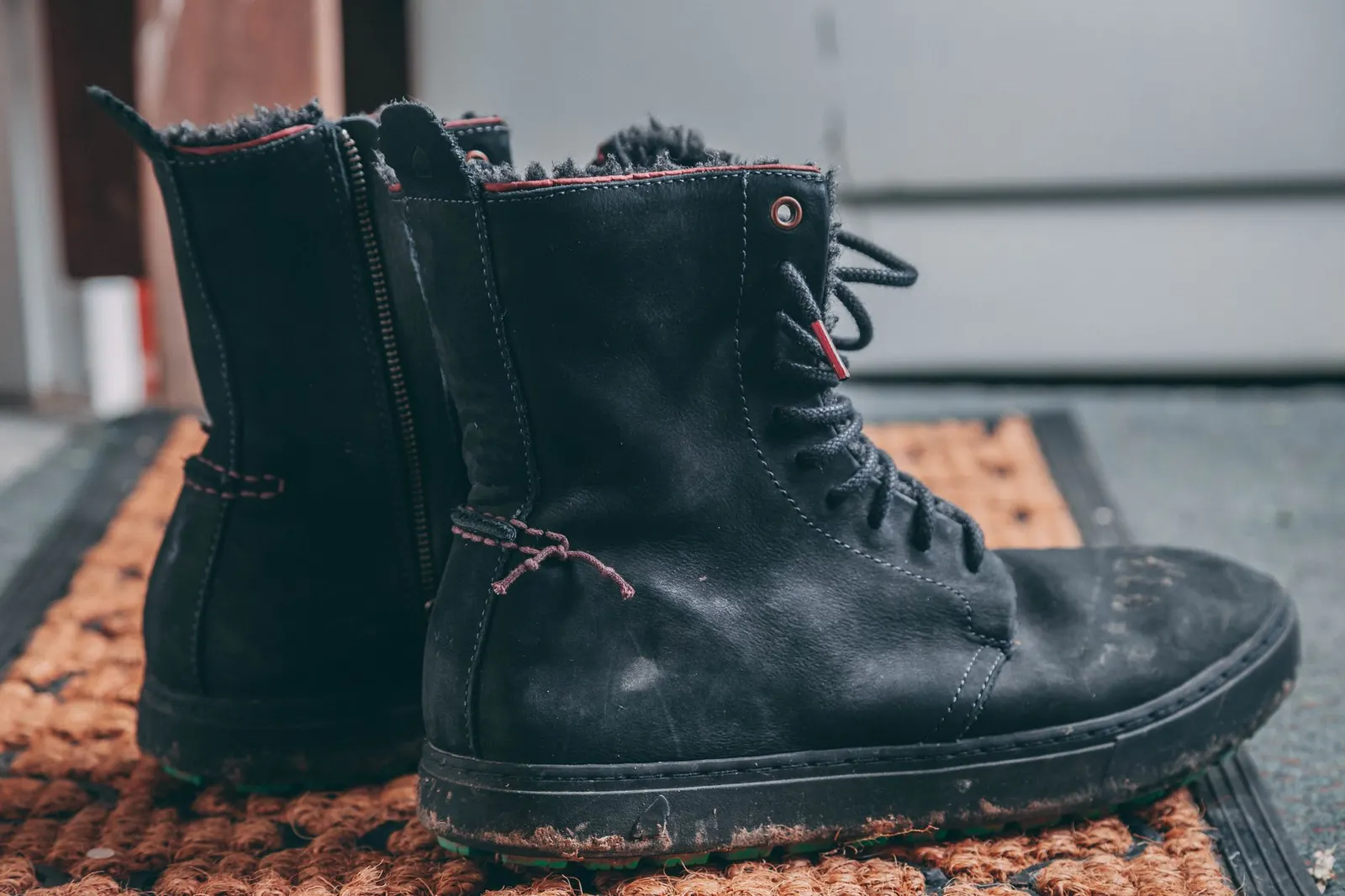 Close-up view of black leather winter hiking boots on a doormat indoors.