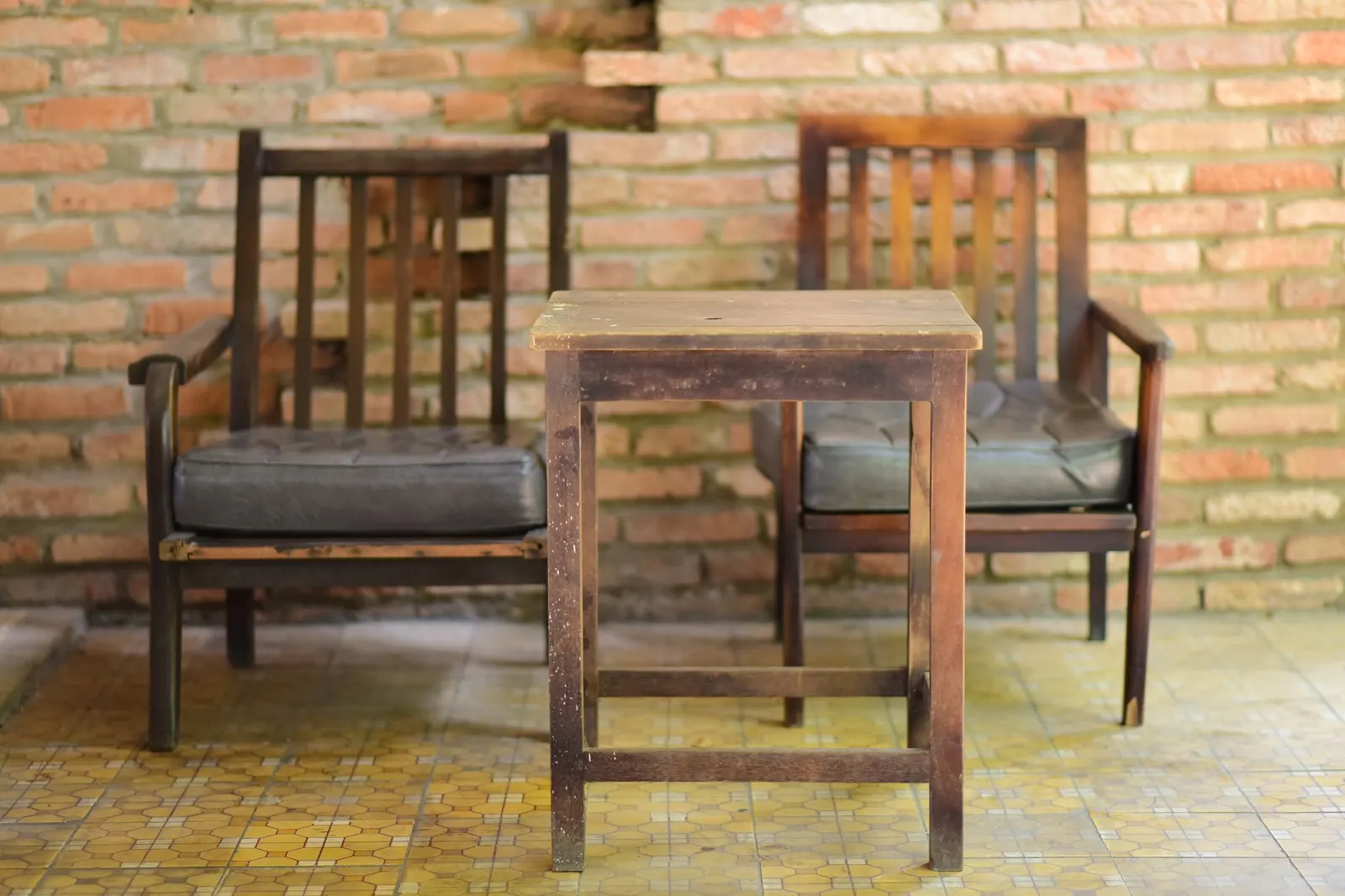 Vintage wooden chairs and table set against a textured brick wall, ideal for rustic decor themes.