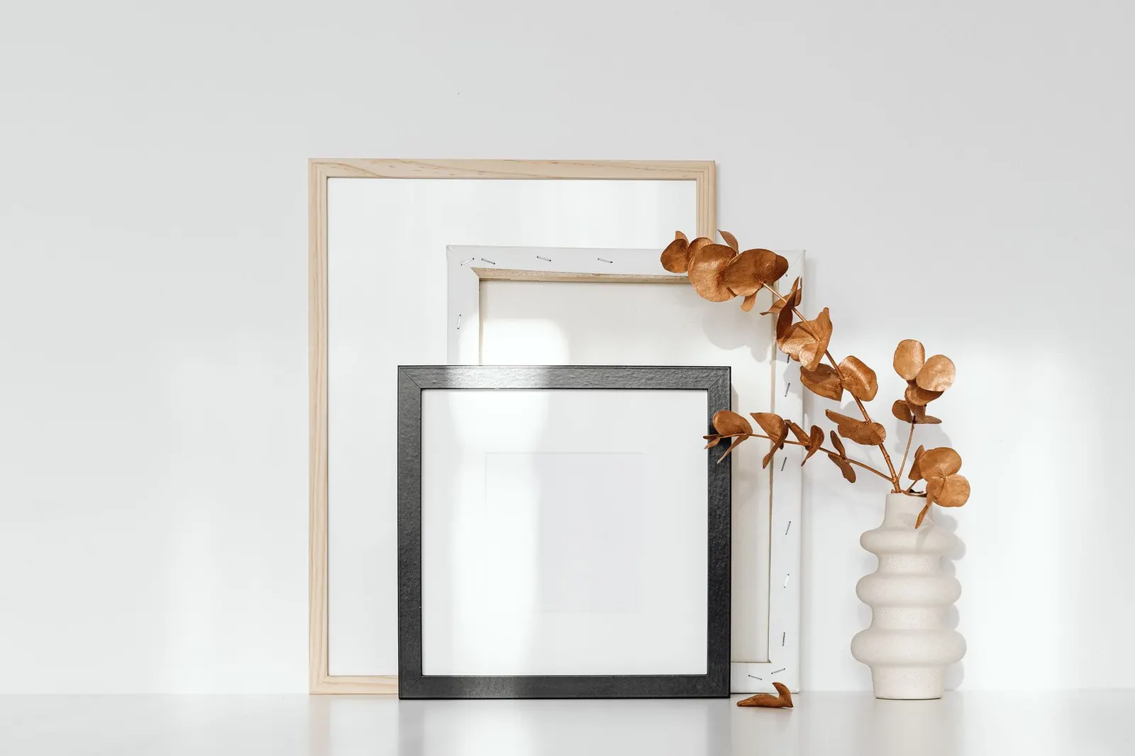 Elegant minimalist composition of picture frames and a white ceramic vase with dried eucalyptus.