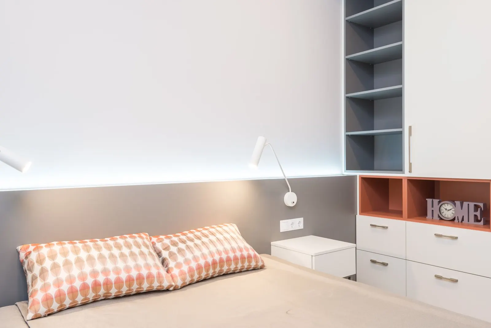 Comfortable bed with cushions and minimalism lamps above nightstands in cozy bedroom with white furniture